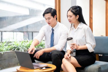 İki iş adamı birlikte çalışıyorlar. Parlak bir ofiste dizüstü bilgisayarda bir projeyi inceliyorlar.