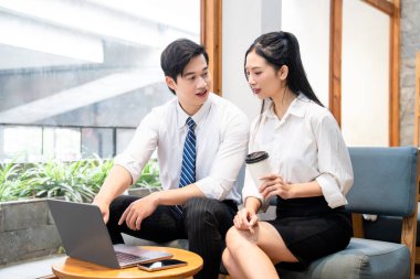 İş kıyafeti giymiş iki genç profesyonel modern bir ofiste dizüstü bilgisayar kullanıyor.