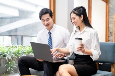 İki genç iş arkadaşı gün içinde bir kafede kahve içerken bir dizüstü bilgisayarla iş birliği yapıyorlar.