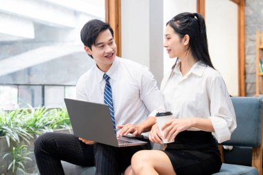 Asyalı iş adamları, modern tasarım ve kahve ile parlak bir ofiste dizüstü bilgisayar üzerinde çalışırken iş birliği yapıyorlar.