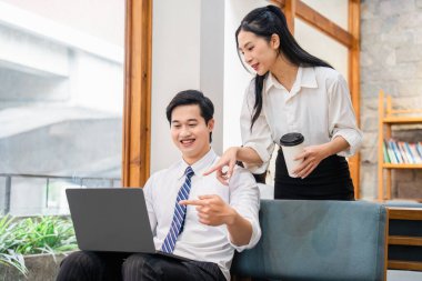 İki ofis arkadaşı birlikte bir dizüstü bilgisayarı inceliyor ve parlak bir alanda fikirleri tartışıyorlar.