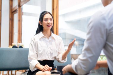 Beyaz tişörtlü bir kadın kafede biriyle konuşurken el kol hareketi yapar.