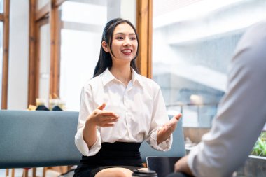İş kıyafeti giyen genç bir profesyonel, ofis ortamında konuşurken coşkulu bir şekilde el kol hareketi yapar.