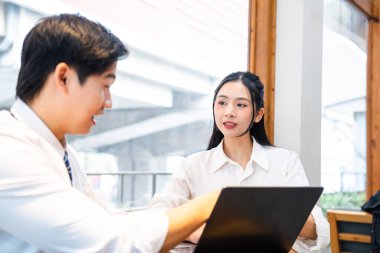 Beyaz gömlekli iki genç profesyonel açık bir dizüstü bilgisayarla modern, parlak bir ofis alanında iş birliği yapıyorlar.