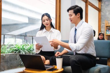 Bir erkek ve bir kadın, yakınlarda bir laptop ve kahve ile aydınlık bir alanda belgeleri gözden geçiriyorlar.