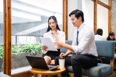 İki profesyonel, parlak bir ofiste, bir dizüstü bilgisayarla belgeleri gözden geçiriyorlar.