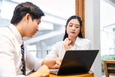 İki iş arkadaşı, kapalı alandaki dizüstü bilgisayara bakarak parlak bir ofis ortamında iş birliği yapıyor.