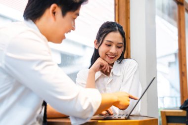 Beyaz gömlekli gülümseyen meslektaşlar parlak bir ofiste dizüstü bilgisayarla birlikte çalışıyorlar.