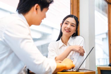 Beyaz tişörtlü bir adam ve kadın parlak bir ofis alanında dizüstü bilgisayarla birlikte çalışıyorlar.