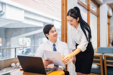Ofiste genç bir adam ve kadın bir dizüstü bilgisayar ve doğal ışık ile kağıtları tartışıyorlar.