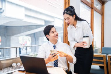 Modern bir çalışma alanındaki iki genç profesyonel iş birliği yapıyor. Biri telefondan diğerine bir şey gösteriyor.