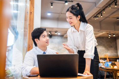 İki genç profesyonel, bir kafede bir dizüstü bilgisayardaki bilgileri incelerken sohbet sırasında gülümsüyor.