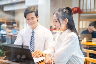 İki iş arkadaşı bir ofis veya kafe ortamında dizüstü bilgisayar kullanırken iş birliği yapıyor. Gülüyorlar.