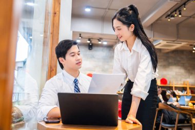 İki iş arkadaşı bir dizüstü bilgisayardaki bilgileri inceleyen bir proje üzerinde birlikte çalışıyorlar.