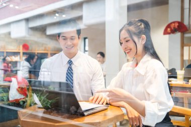 İki iş arkadaşı bir kafede dizüstü bilgisayarla iş birliği ve ortak çalışma alanı kullanımını öneriyor.