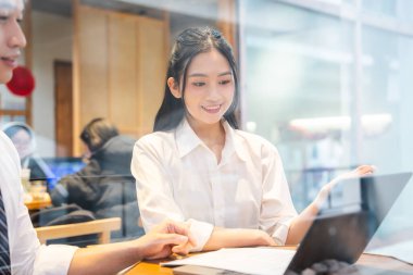 Ofiste iki meslektaş bilgisayarla ve belgelerle bir dizüstü bilgisayar üzerinde çalışıyor.