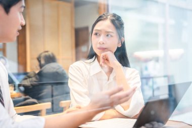 Asyalı kadın, iş arkadaşı ile iş görüşmesi sırasında çenesini dikkatle dinlendiriyor.