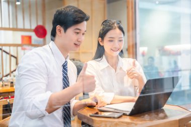 İki gülümseyen meslektaşı bir dizüstü bilgisayarda çalışıyor ve baş parmak hareketleriyle olumlu geri bildirim yapıyorlar.