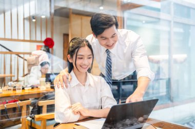 Gülümseyen meslektaşlar, gündelik bir atmosferi olan, modern ve parlak bir çalışma alanında bir dizüstü bilgisayarın üzerinde iş birliği yapıyorlar.