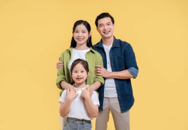 Sarı arka planda poz veren mutlu üç kişilik aile anne ve baba kızlarının etrafını sardı.