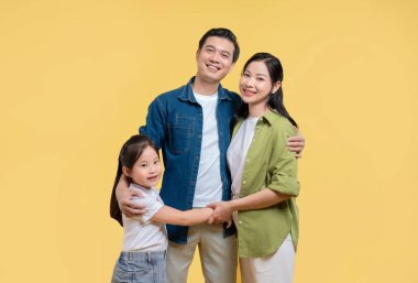 Sarı bir arka planda poz veren mutlu bir aile. El ele tutuşurken gülümsüyor.