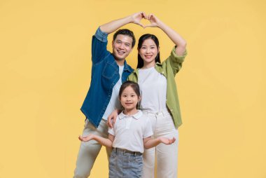 Üç kişilik bir aile, kolları sarı bir zemin üzerinde mutluluk ve sıcaklık saçan bir ev şekli oluşturur.