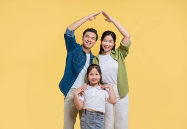 Gülümseyen aile, elleri sarı bir zemin üzerinde güvenlik ve birlikteliği simgeleyen bir ev yaratıyor.