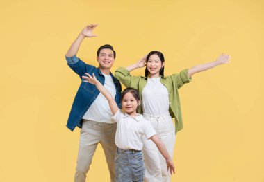 Üç kişilik mutlu bir aile. Aralarında genç bir kız da var. Katı sarı bir zemine karşı kollarını açmış poz veriyorlar.