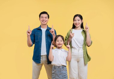 Mutlu Asyalı bir ailenin, bir çocukla gülümseyen, sarı arka planı gösteren bir stüdyo fotoğrafı.
