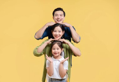 Üç kişilik gülümseyen bir aile, sarı arka planlı bir stüdyoda üst üste yığılır.