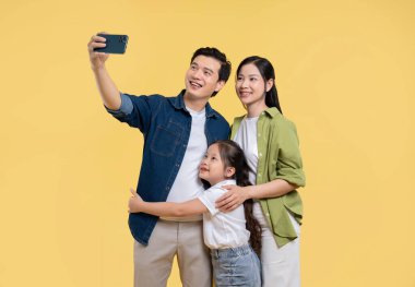 Üç kişilik gülümseyen bir aile, sarı bir arkaplan önünde selfie için birlikte poz verirler. Mutludurlar.