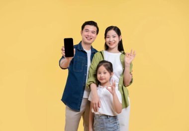 Üç kişilik gülümseyen aile sarı arka planda boş ekranlı cep telefonu gösteriyor.