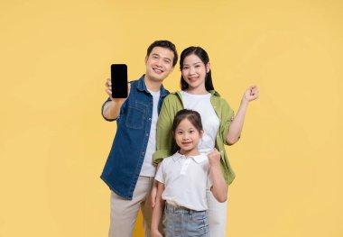 Üç kişilik mutlu bir aile, elinde cep telefonu tutan parlak sarı bir arka planda duruyor.