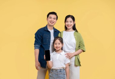 Bir aile mutlu bir şekilde gülümsüyor. Kız, birlik olduğunu gösteren canlı sarı bir arka plana karşı akıllı bir telefon tutuyor.