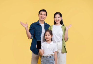Üç çocuklu mutlu bir Asyalı aile sarı arka planda bir akıllı telefon sunar.