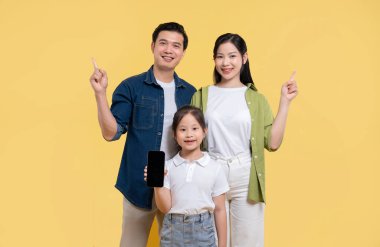 Gülümseyen bir anne baba ve kızı sarı bir arka planda birlikte poz veriyorlar.