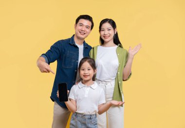 Üç kişilik bir aile sarı zemine karşı gururla ve mutlulukla gülümseyen bir cep telefonu gösteriyor.