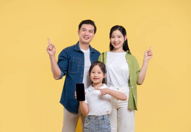 Üç kişilik bir aile, sarı arkaplanda gülümseyen bir cep telefonu uygulamasını gösteriyor.