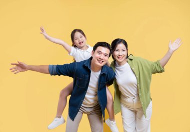 Sarı arka planda günlük giysiler içinde neşeli aile portresi.