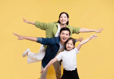 Mutlu bir aile, sarı bir arka planda kollarını açıp gülümseyerek uçuşu taklit eder.