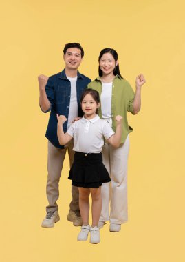 Anne, baba ve kızları da dahil mutlu bir aile sarı bir arka planda gülümseyerek yan yana dururlar.