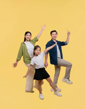 Asyalı aile: anne baba ve kızı gülümsüyor ve basit sarı bir stüdyo geçmişine karşı birlikte poz veriyorlar.