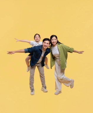 Üç kişilik neşeli bir aile stüdyoda mutluluk ve sıcaklık saçan sarı bir arkaplanda poz veriyor.