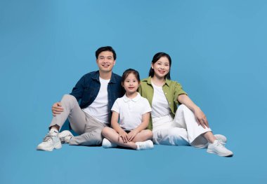 Neşeli genç ebeveynlerin ve kızlarının portresi. Stüdyoda mavi, pürüzsüz arka planda oturuyorlar.