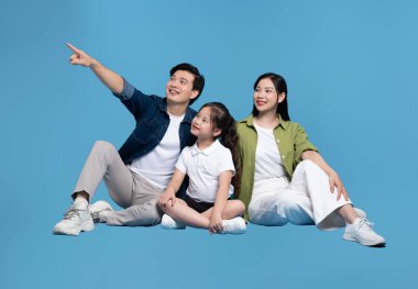 Mavi bir yüzeyde oturan Asyalı üç kişilik aile gökyüzüne doğru bakıyor.