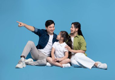 Üç kişilik neşeli bir aile mavi bir arka planda yan yana oturup gülümserken baba yan tarafı işaret ediyor.