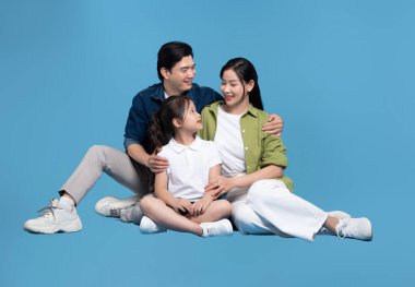 Genç, mutlu bir aile gülümser ve mavi bir arka planda birlikte oturur neşe ve beraberlik saçar.