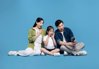 Mobil cihaza bakan anne ve baba sürpriz bir şekilde mavi arka planda oturuyorlar.