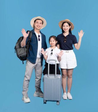 Tatile hazır üç kişilik aile gülümsüyor ve mavi bir arka planda bavulla yaz giysileri içinde dalgalar var.