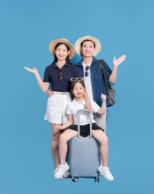 Bir aile mavi bir zemine karşı duruyor. Tatile hazır. Kızım bavulda gülümsüyor.